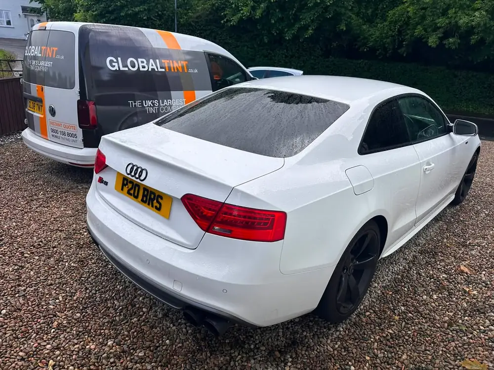 White Audi S5 with dark rear glass, parked on gravel beside a Global Tint van