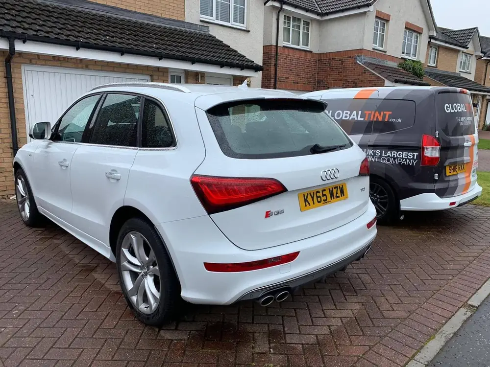 White Audi SQ5 with tinted rear windows, parked on a paved driveway beside a Global Tint van.