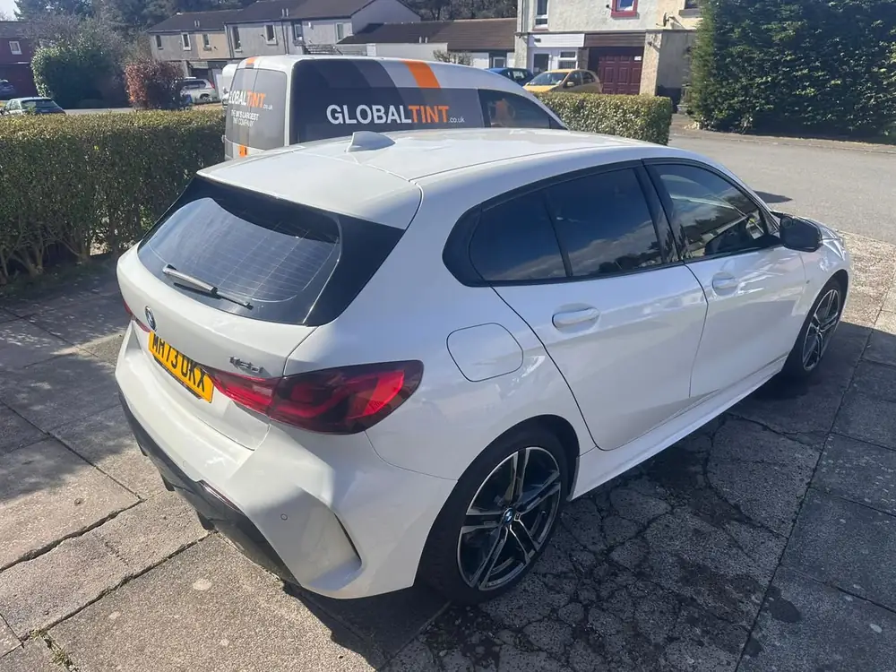 White BMW 1 Series with dark rear side windows and rear windscreen, parked beside a Global Tint van