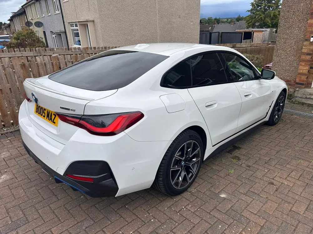 White BMW i4 with dark rear side windows and back windscreen, parked on a brick driveway.
