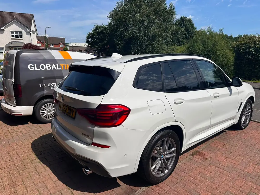 White BMW X3 with dark rear side windows and rear windscreen, parked beside a Global Tint van