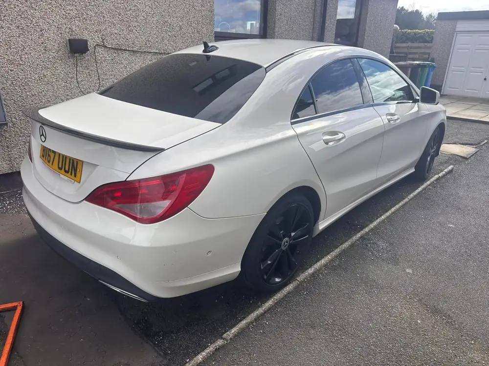 White Mercedes-Benz CLA with dark rear side windows and back windscreen, parked beside a house.