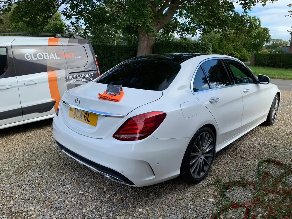 White saloon with dark rear side windows and back windscreen, parked on gravel beside a Global Tint van.