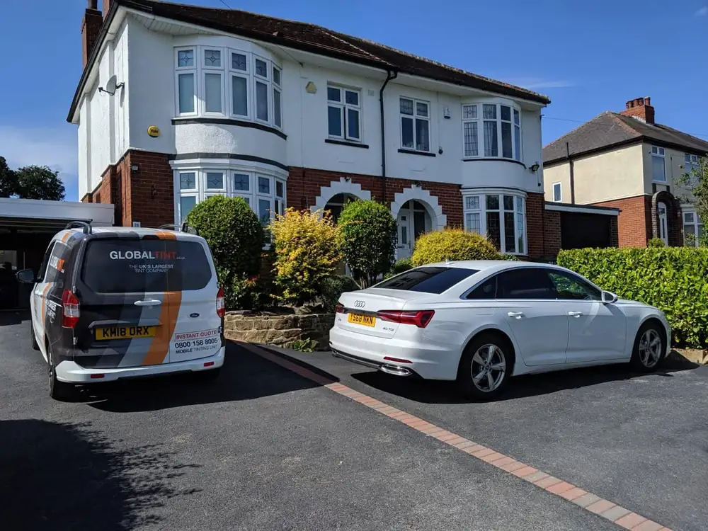 White saloon with dark rear glass, parked on a driveway beside a Global Tint van