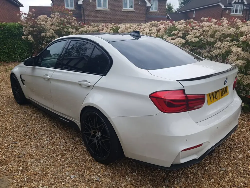 White saloon with dark rear side windows and rear windscreen, parked on gravel beside a hedge.