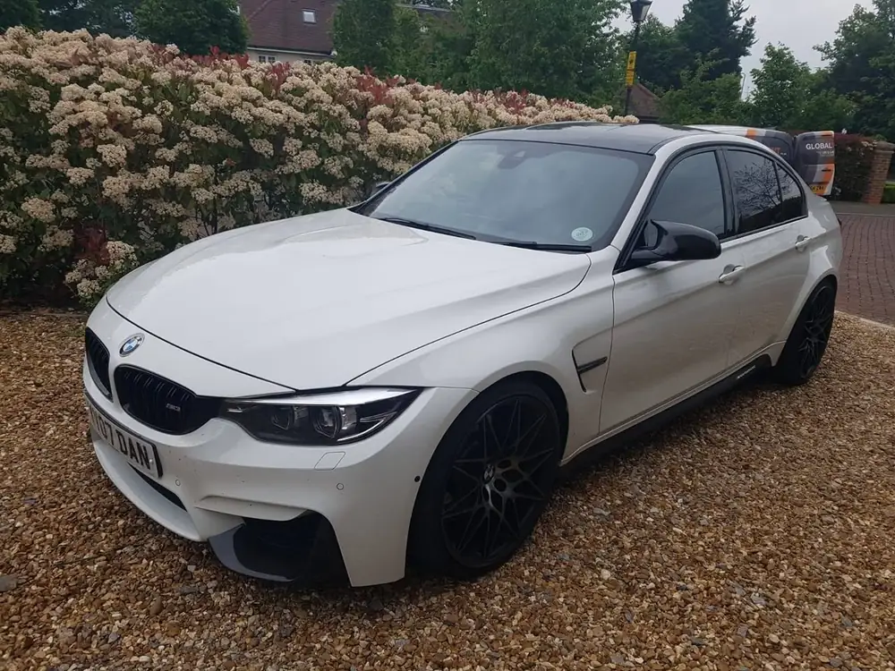 White saloon with its rear side window tinted dark and black wheels, parked on gravel