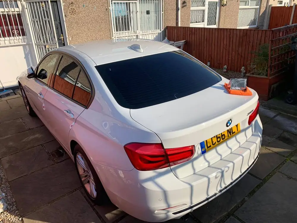 White BMW saloon with dark rear side windows and rear windscreen, viewed from behind on a paved driveway