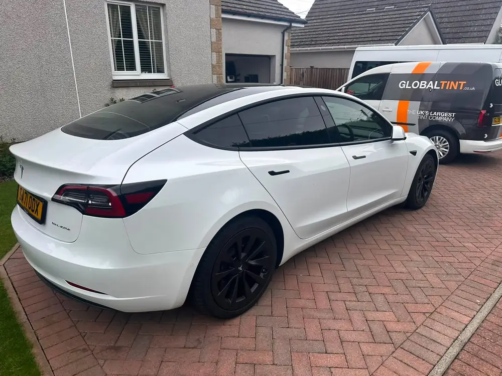 White Tesla Model 3 with dark rear side windows and rear windscreen, parked on a block-paved driveway