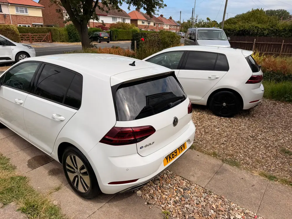 Two white Volkswagen Golfs with dark rear side glass; foreground e-Golf also shows its dark back windscreen.
