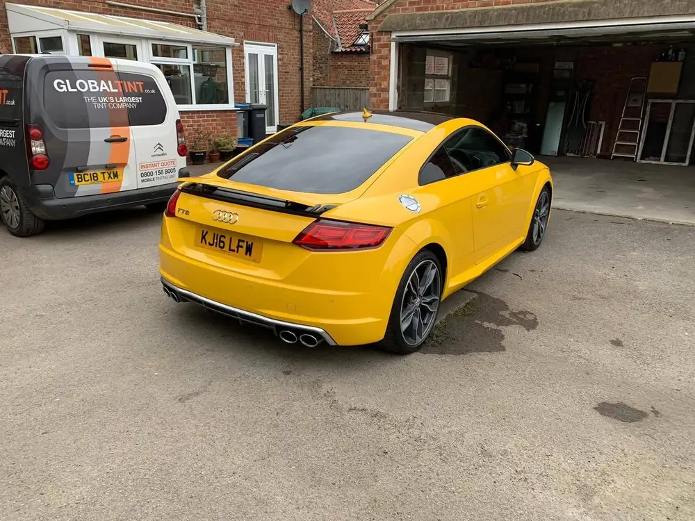 Yellow Audi TTS with dark rear glass, parked outside an open garage beside a Global Tint van